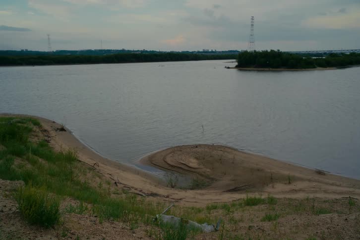 A tranquil view of a wide, flowing river with a sandy bank and a distant island on a cloudy day