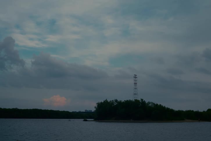 A serene view of an island with an electrical tower surrounded by water under a cloudy evening sky