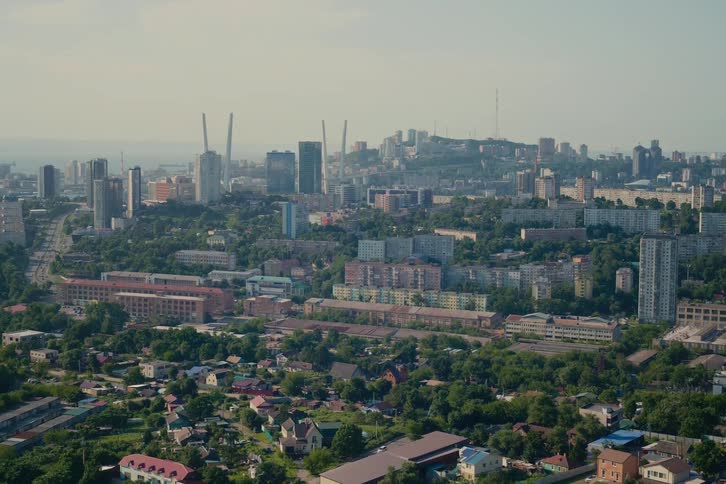 A wide, static shot of the sprawling cityscape of Vladivostok, Russia, on a hazy summer day