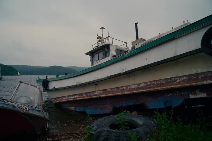 An old, rusty fishing boat is beached on the shore of a lake on a gray, cloudy day