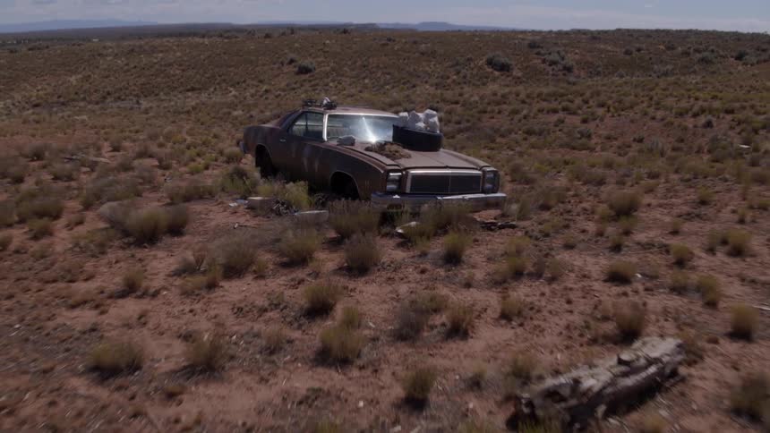 A beat up old car piled with junk sits in a desert area