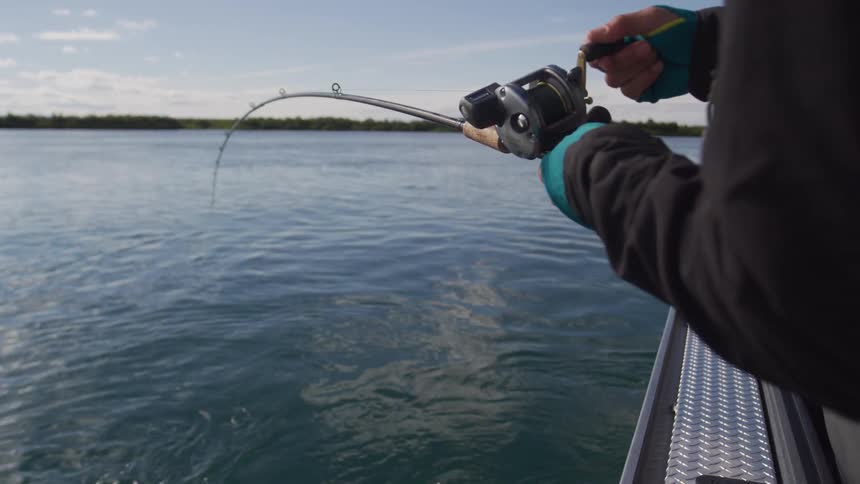 A fisherman on a boat reels in a fish with a bent rod in slow motion