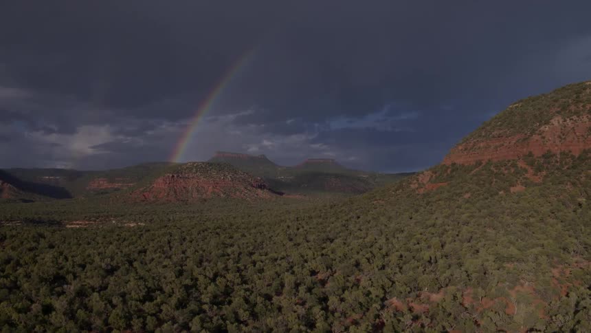 A rainbow arcs up from a hill into the clouds
