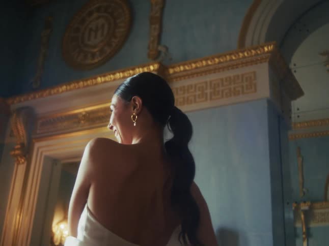 A smiling woman in a beautiful dress playfully covers the camera with a white sheet while in a luxurious classical room