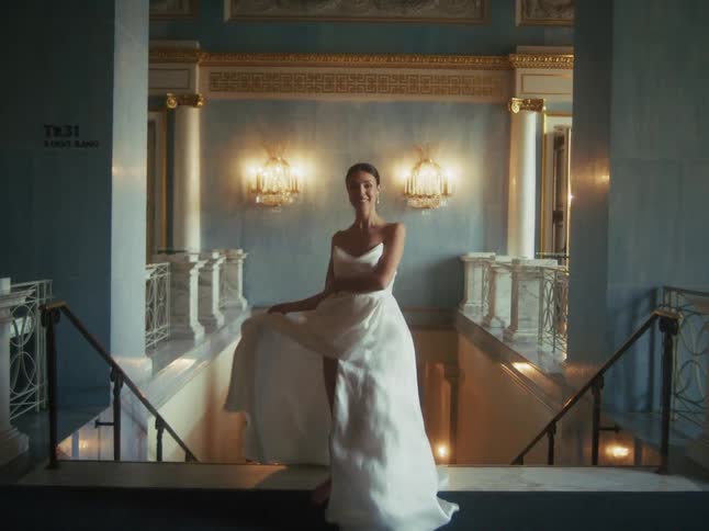 An elegant woman in a flowing white dress twirls gracefully on a grand marble staircase