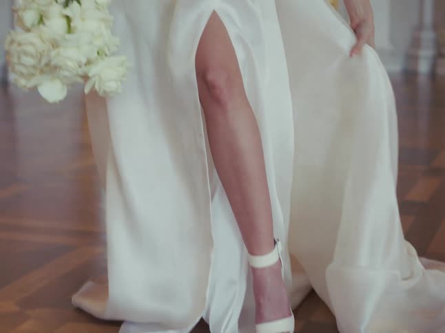 An elegant bride shows off her white sandal through the slit of her flowing wedding dress while holding a beautiful bouquet of white roses