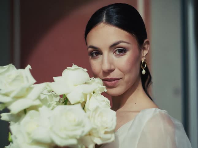 A close-up portrait of a stunning bride gently smiling while smelling her beautiful white rose bouquet