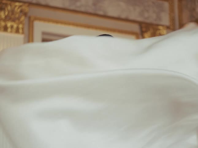 A stunning bride in an elegant white gown smiles softly while posing in a magnificent, gold-accented room