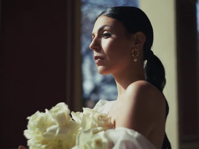 An elegant bride in profile holds a bouquet of white roses, bathed in the gentle morning sunlight
