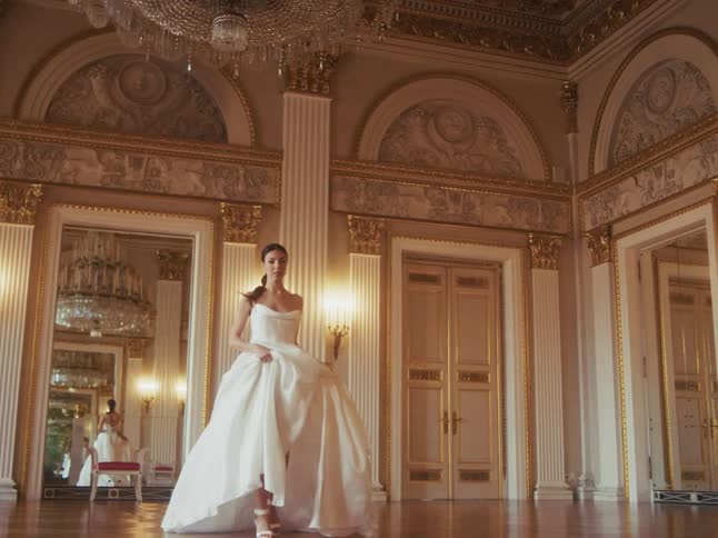 A beautiful bride in a flowing white gown walks towards the camera in slow motion through a luxurious grand ballroom