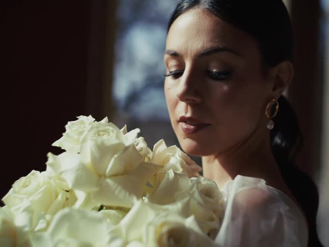 An elegant bride in a white gown holds a beautiful bouquet of white roses, looking serenely into the sunlight