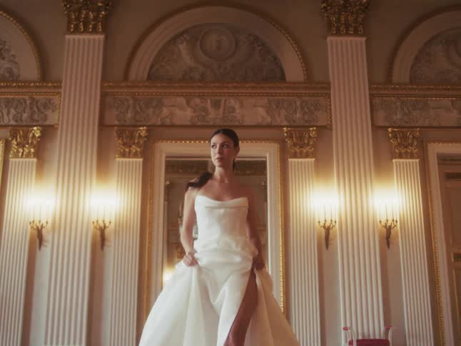 A beautiful bride in a white gown poses dramatically in a luxurious ballroom as the camera pulls away in slow motion