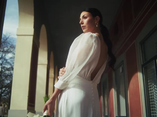 A stunning bride in an elegant white dress with sheer puff sleeves poses gracefully in a sunlit classical colonnade