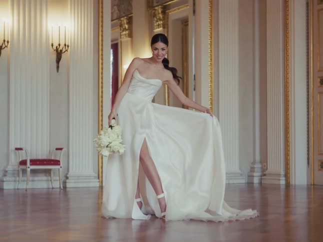Cinemagraph of an elegant bride posing in a luxurious hall, her stunning white wedding dress flowing gracefully as she holds a bouquet of white roses