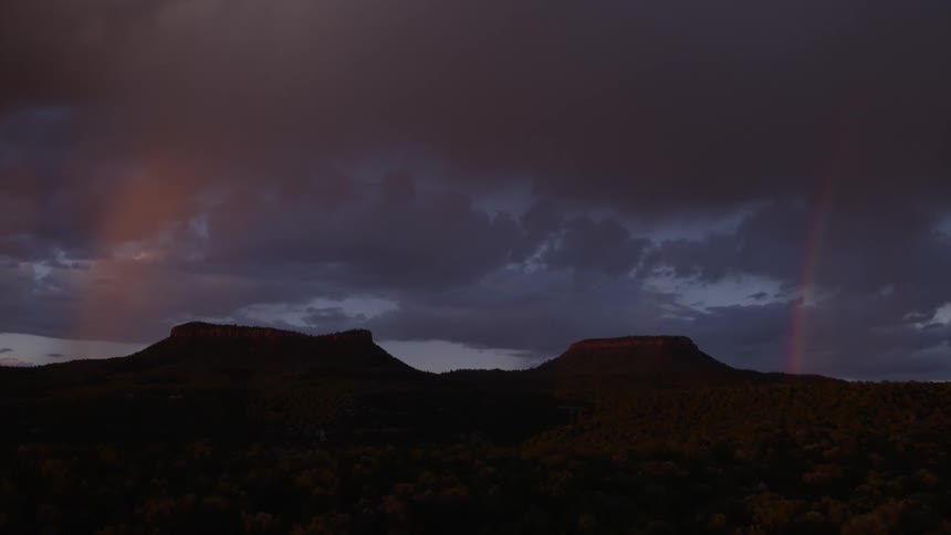 A rainbow arcs up from the landscape into the dark clouds