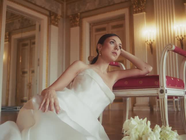 An elegant bride in a beautiful white wedding dress poses gracefully in a luxurious, sun-drenched palace hall
