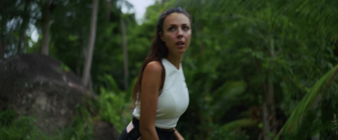 A terrified woman running through a dense jungle stops abruptly to catch her breath, looking around in fear