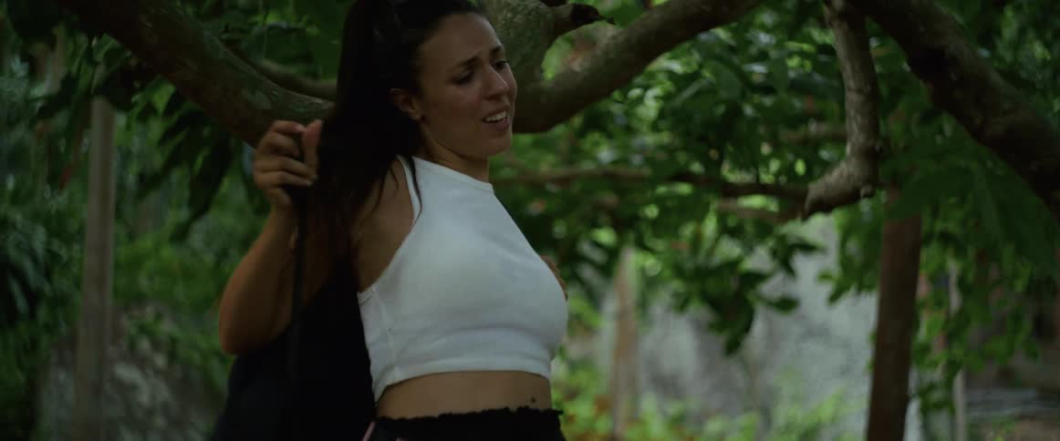A terrified woman wearing a backpack frantically runs through a dense jungle, escaping an unseen threat