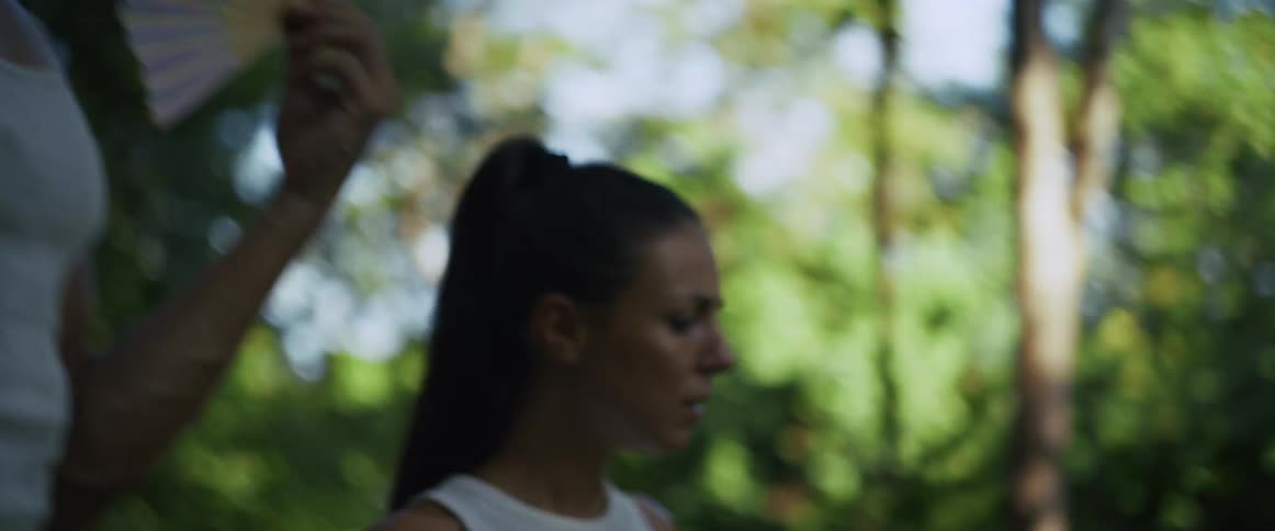 A determined woman with an intense expression runs through a lush green forest in slow motion