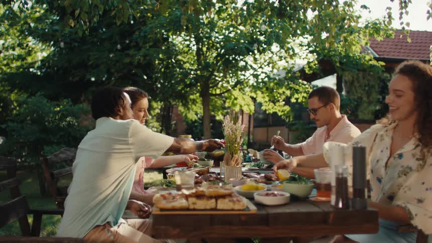 Diverse friends share a delightful al fresco lunch together in a lush green garden on a sunny afternoon