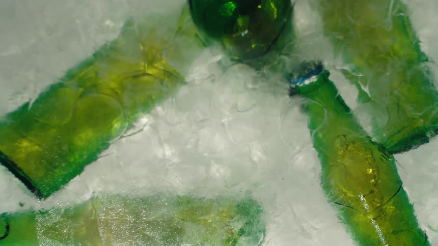 A woman's hand with red nail polish pulls a green beer bottle from a cooler full of melting ice in this mesmerizing time-lapse shot