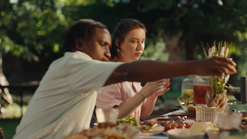 A diverse group of friends laugh and share a vibrant meal together outdoors in a sunlit garden