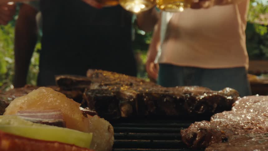 Macro shot pulling back from a large steak to reveal a full grill with burgers, steaks, and vegetables at a backyard barbecue