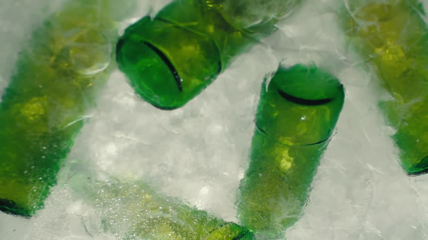 A woman's hand with red nails reaches into a cooler of melting ice filled with green glass bottles