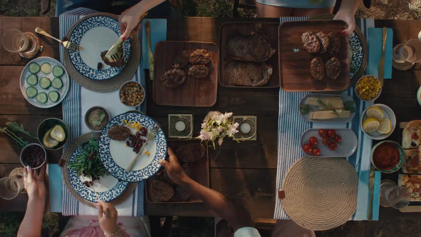 Overhead shot of a group of friends serving themselves from a large spread of food at an outdoor dinner party