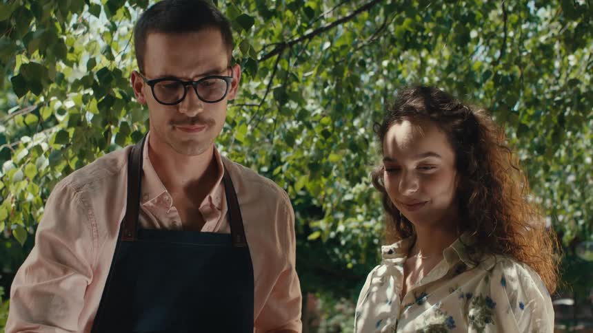 A slow-motion reveal from a low angle shows a smiling couple enjoying a sunny day barbecue in the backyard