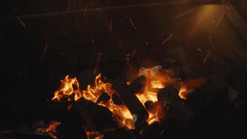 Intense close-up of glowing charcoal embers sending sparks flying as they ignite into a roaring fire