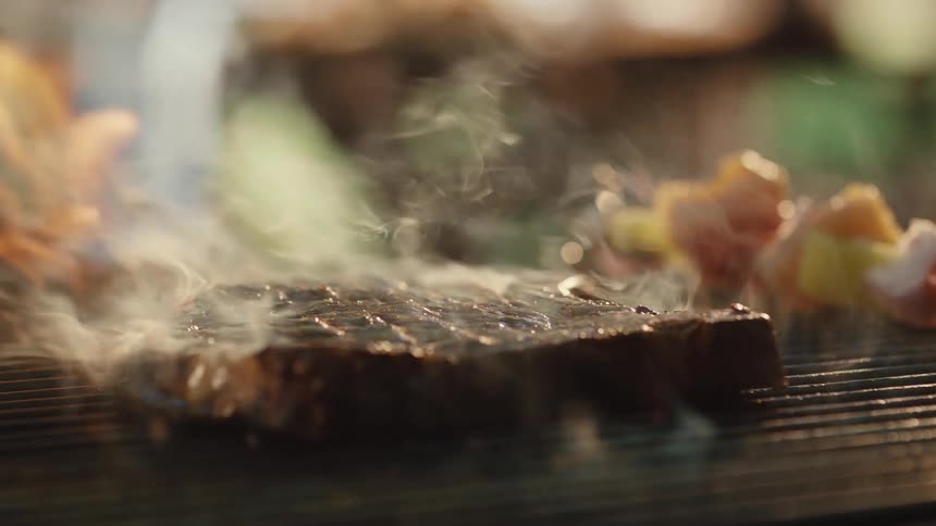 A juicy steak sizzles and smokes on a fiery barbecue grill before being flipped in dramatic slow motion