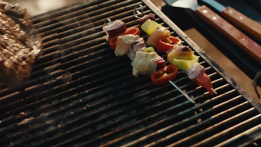 Juicy steaks, burgers, and vegetable skewers sizzle over flames on a barbecue grill in slow motion