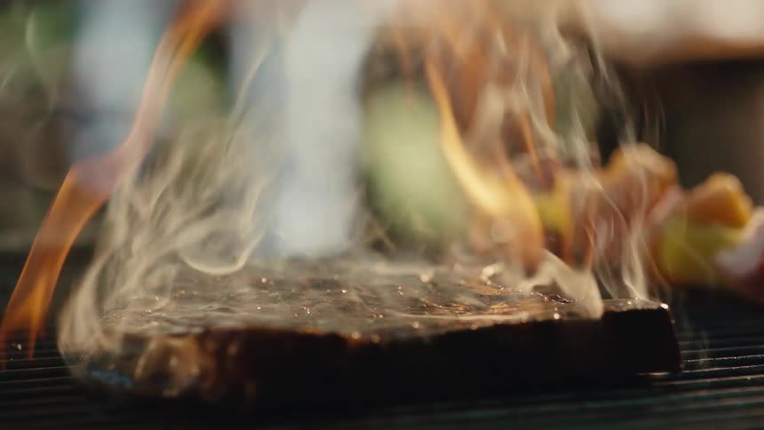 Extreme close-up of a juicy steak and vegetable skewer sizzling over open flames on a hot barbecue grill in slow motion