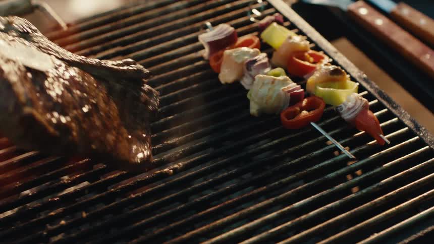Close-up of a variety of meats and vegetable skewers cooking on a flaming barbecue grill