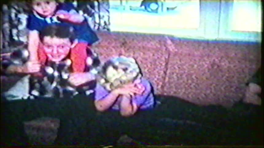 A nostalgic home video captures three playful siblings sitting together on a couch in their living room