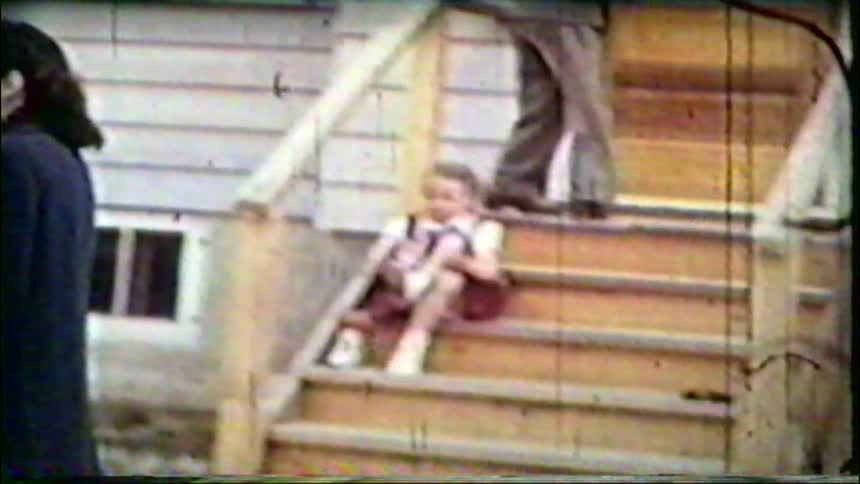 Vintage 1940s home movie shows a soldier in his uniform standing with his wife outside their home while their daughter sits on the stairs