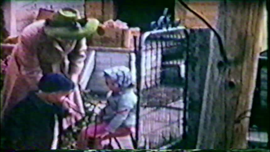 Vintage footage shows a man and two small children looking at an animal cage in a rustic backyard setting