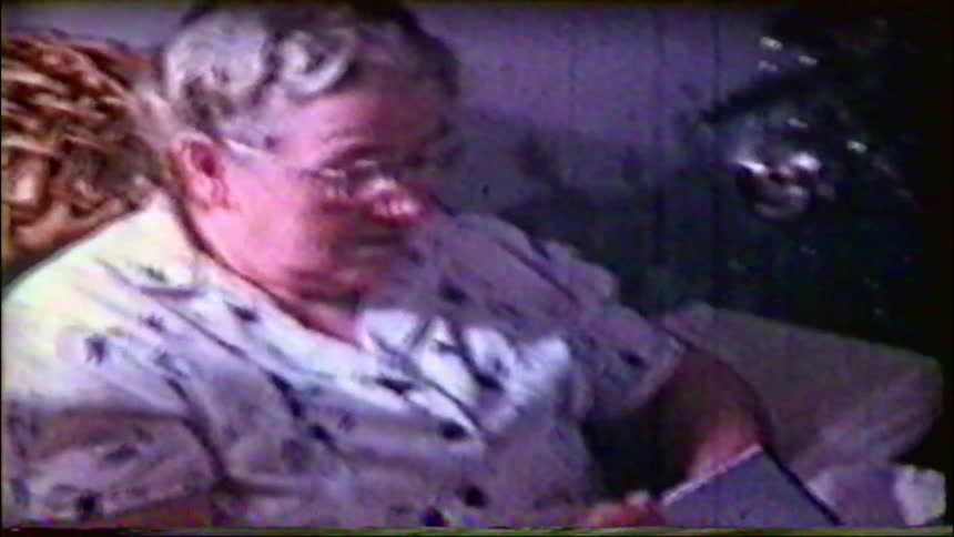An elderly woman reads a card while opening a Christmas present in this nostalgic vintage footage