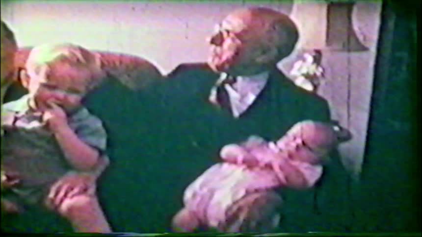 Vintage 8mm footage captures a heartwarming family portrait of a grandfather with his young grandson and a newborn baby