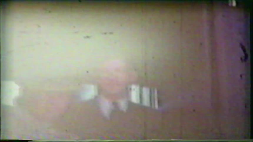 A smiling older couple in formal attire poses for the camera in a grainy, damaged vintage home movie from the 1940s