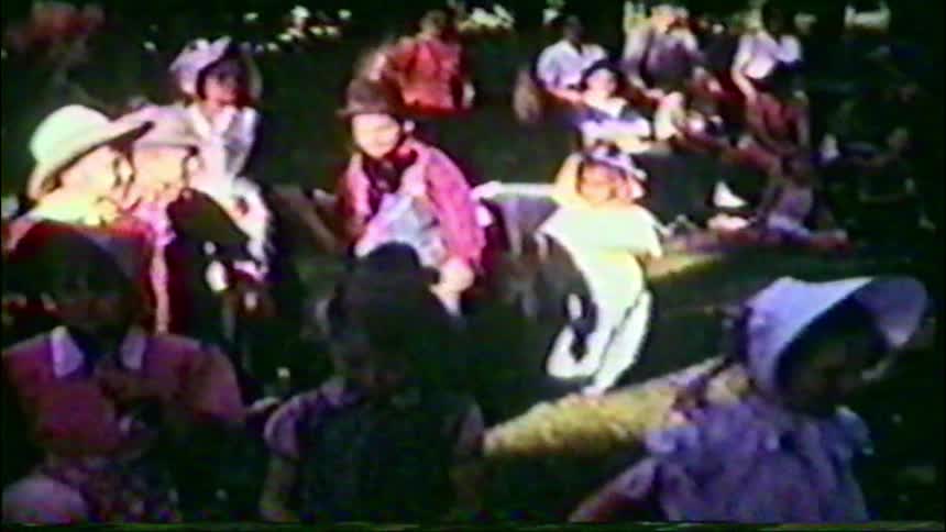 Grainy home movie footage shows a group of children in western costumes at an outdoor event