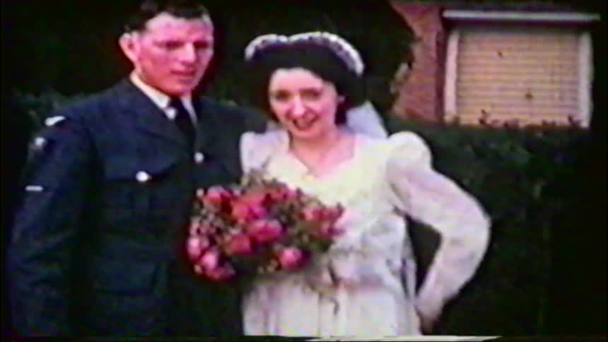 A vintage home movie captures a smiling bride and her groom in a military uniform on their wedding day