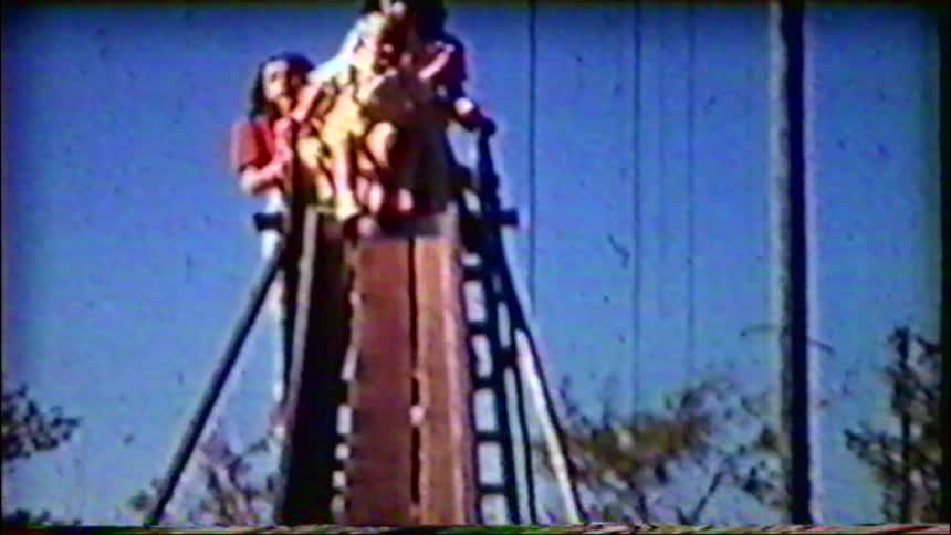 A group of friends anxiously awaits their turn at the top of a giant slide in grainy vintage footage