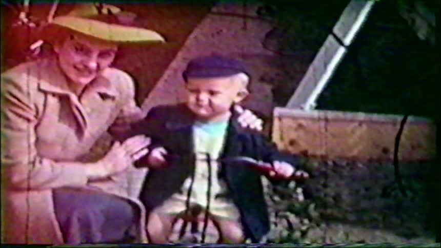 Charming vintage footage from the 1950s shows a proud mother and her young son posing with his tricycle in the garden