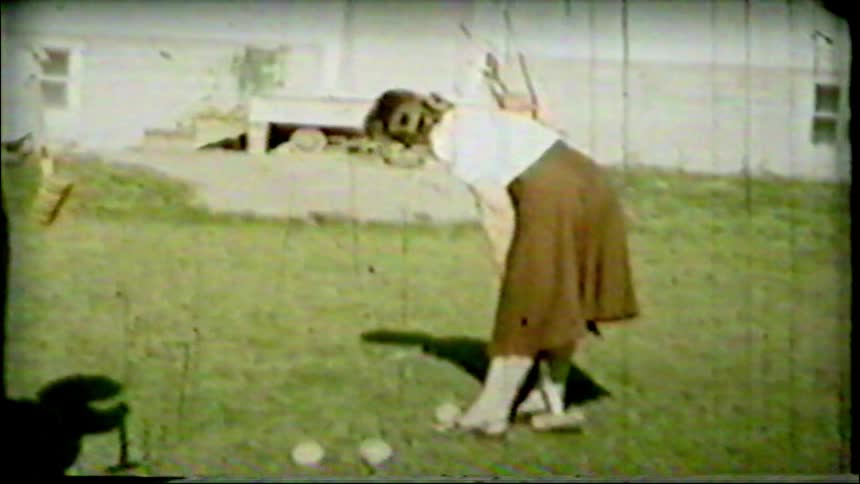 Archival 8mm footage from the 1950s shows two young women and a small dog playing a game of croquet in their backyard