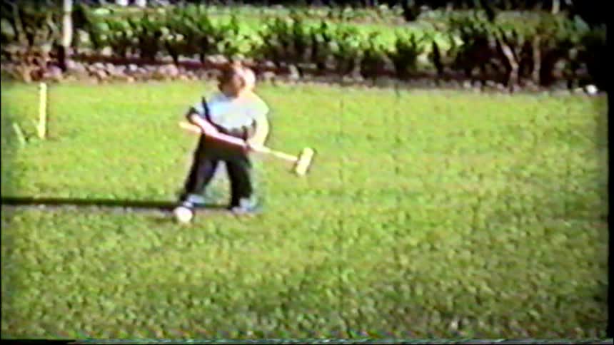 A determined toddler in overalls learns to play croquet on the lawn in this charming vintage footage