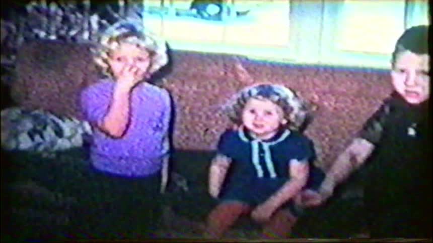 A nostalgic home movie from the 1950s shows a father and his children sitting together on the living room couch