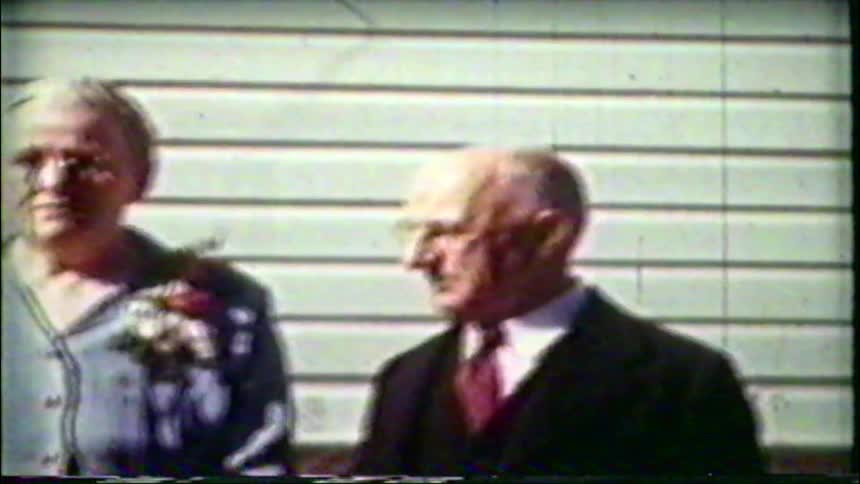 An elderly couple in their Sunday best pose for a portrait in a vintage home movie from the 1950s