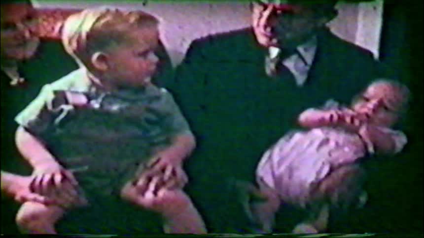 Proud grandparents pose with their toddler grandson and newborn grandchild in a heartwarming vintage home movie